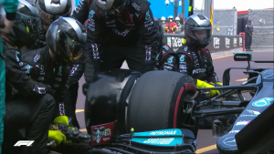 Mechanicy Mercedesa w czarnych kombinezonach próbują wymienić oponę z bolidu podczaś wyścigu